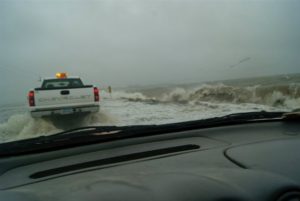 Two trucks travel through shallow water on highway 57.