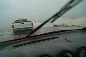 Two trucks travel through shallow water on highway 57.